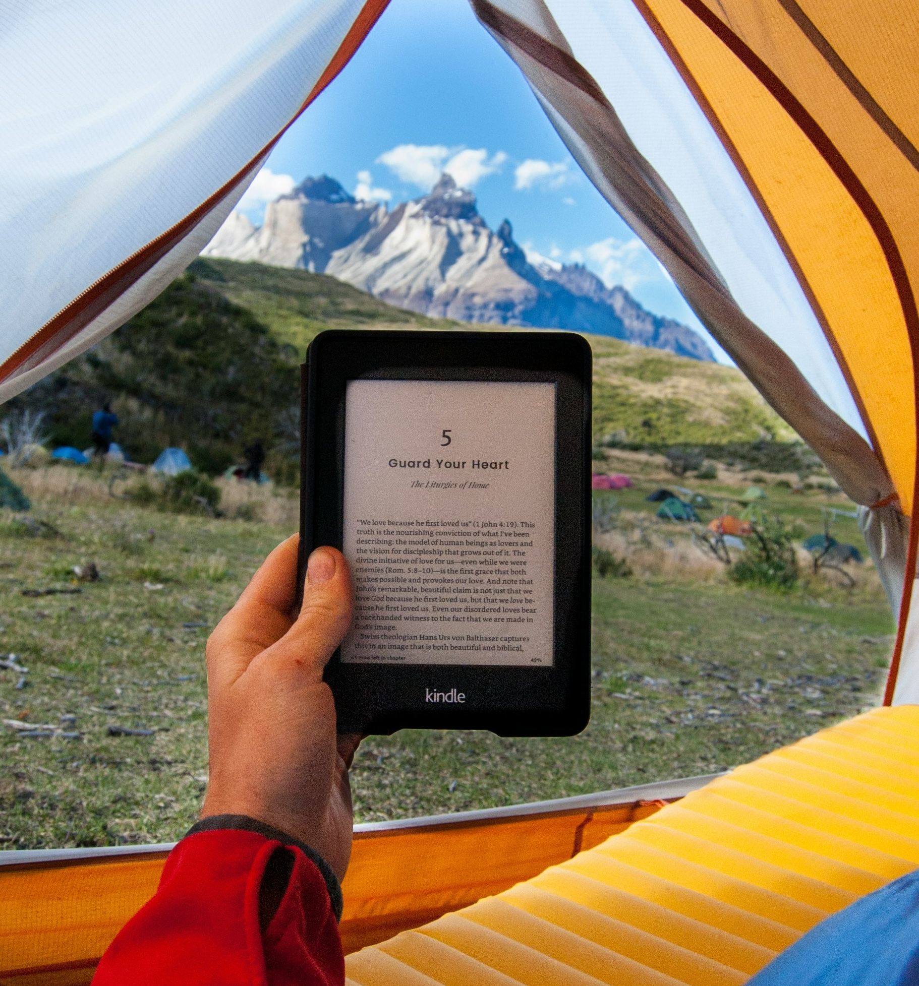Person reading an ebook while camped on a mountainside.
